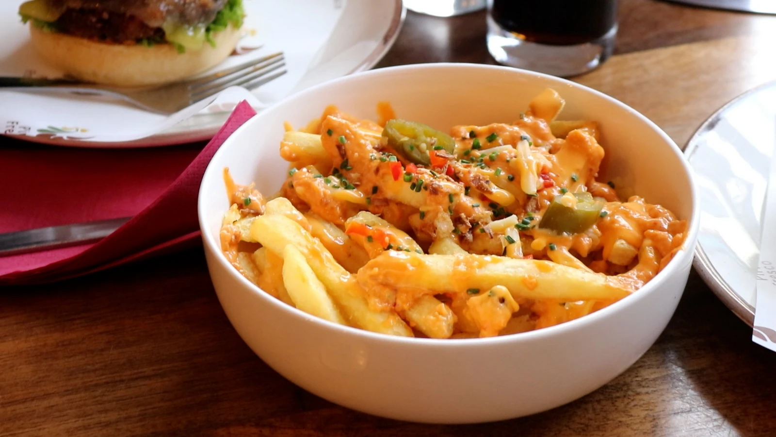 Loaded fries with cheese sauce and jalapeños, a burger behind